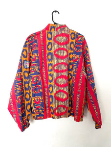 Bomber jacket with an allover red, orange and blue colorful Ikat print. Jacket has two front pockets and front zipper with elastic on wrists and waist. 